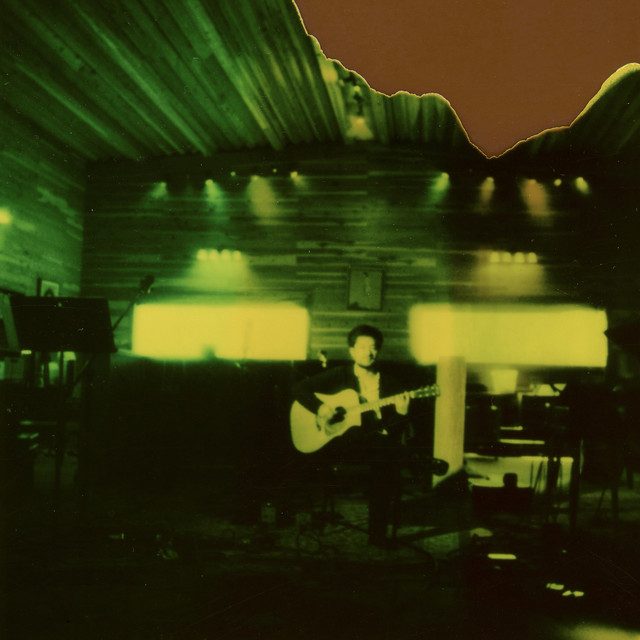 Portada de Niña Bonita (Acústico): Dstance tocando guitarra en un estudio con luces verdes