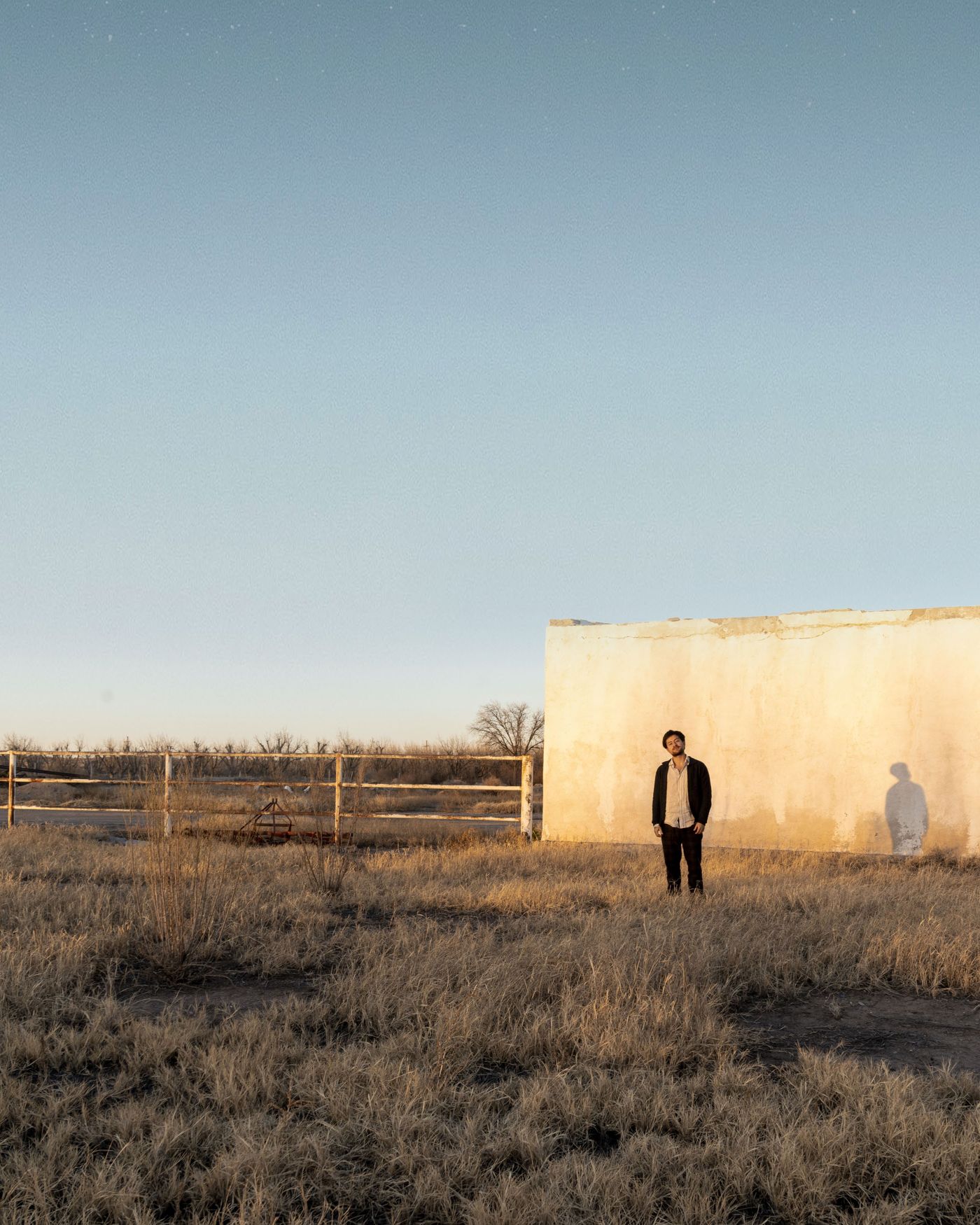 Dstance de pie en un campo seco frente a un muro blanco, con el cielo al atardecer (foto del press kit)