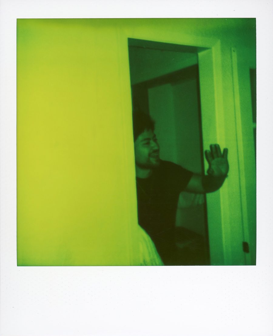 Polaroid verde de un músico saludando con la mano desde una puerta