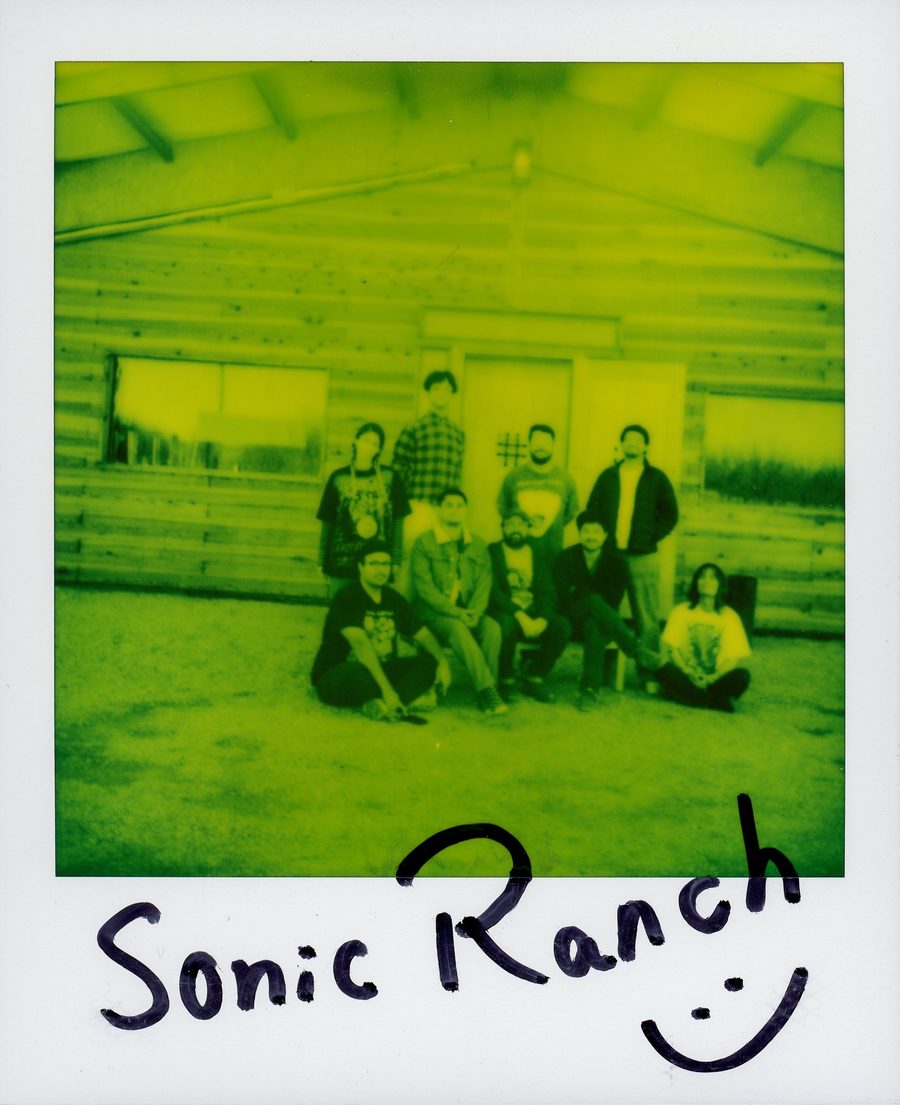 Polaroid en verde y amarillo de la banda frente a la cabaña de Sonic Ranch, con «Sonic Ranch» y una carita escritos a mano